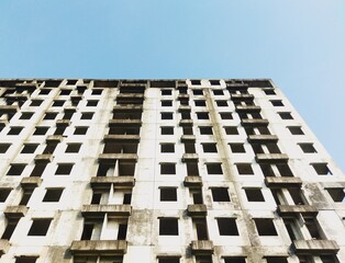 Abandoned high-rise building under clear blue sky. Urban decay with modern architecture lines,...