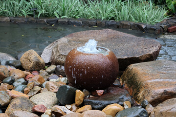 Round stone bowl water feature fountain encircled by rocks in a garden