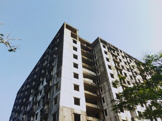 Tall abandoned apartment building with exposed concrete and no windows, viewed from below. Urban...