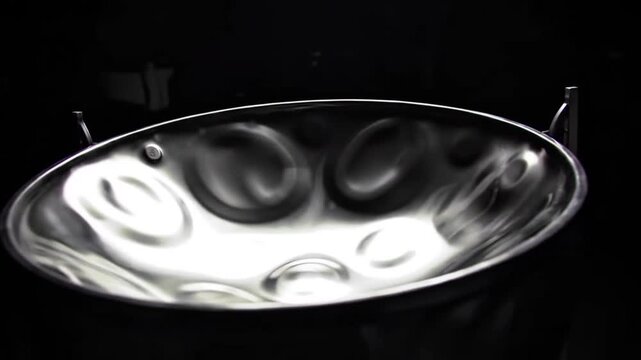 Close-up of a gleaming chrome steelpan, a melodic percussion instrument integral to Caribbean music, showcasing its unique indented notes against a stark black background