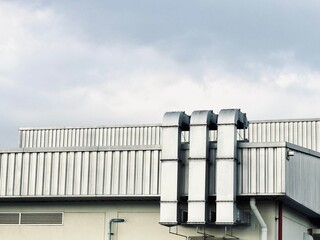 The image shows the top of a modern factory building with multiple large, metallic ventilation ducts rising against a cloudy sky.