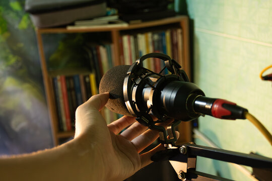 A professional condenser microphone on a stand in a home studio with a bookshelf background. Concept of podcasting and audio production
