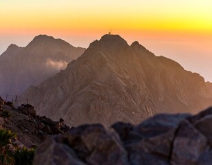 Sunset illuminates a rugged mountain peak, layers of rock visible, foreground rocks in shadow