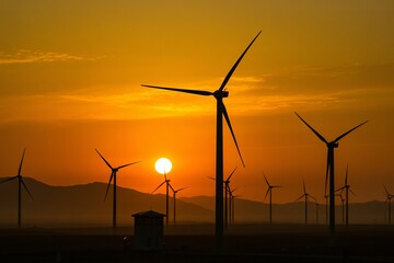 Obraz premium Wind turbines at sunset over mountains, renewable energy, wind power farm, clean electricity, sustainability.