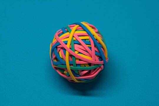 Colorful rubber band ball on blue background, office supplies, elasticity, stress relief, minimal design.