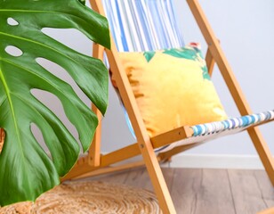 Wooden deck chair with striped fabric, yellow cushion, and large tropical leaf beside it on a jute mat