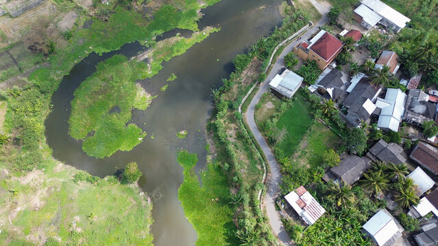 Drone shot of a riverside village with houses, curved waterway, and lush green vegetation surrounding the area.