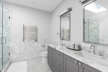 A bathroom with a large grey vanity cabinet, marble tiled walls and flooring, chrome faucets on a...