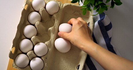 Closeup of taking fresh egg from open carton on wooden table with striped towel, top view breakfast...