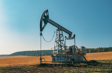 A large oil pump jack operates in an open field, extracting crude oil