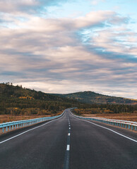 A long, open highway leads through a picturesque mountainous area.
