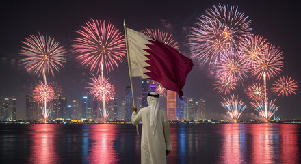 Person Wearing Traditional Middle Eastern Clothing Holding Qatar Flag with Fireworks Display Over City Skyline at Night