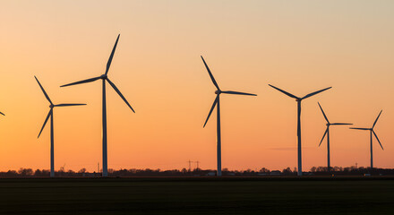Fototapeta premium Wind Turbines Silhouetted Against Colorful Sunset Sky Over Open Field