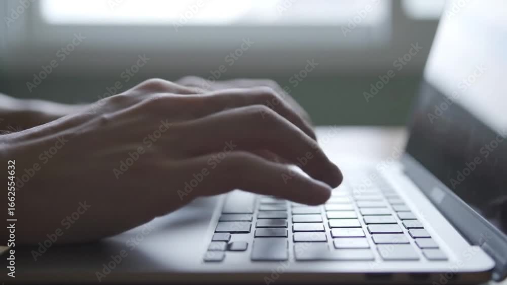 Poster person typing on silver laptop computer keyboard in front of window