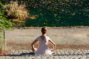 High resolution picture of a young woman in a white dress sitting by the stone steps at Laurelhurst Park lake, facing the water filled with floating autumn leaves, creating a calm seasonal scene