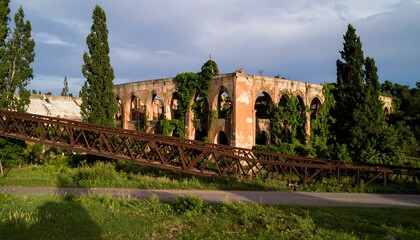 Rustic brick ruin with arched openings, overgrown with vegetation, and a metal footbridge nearby