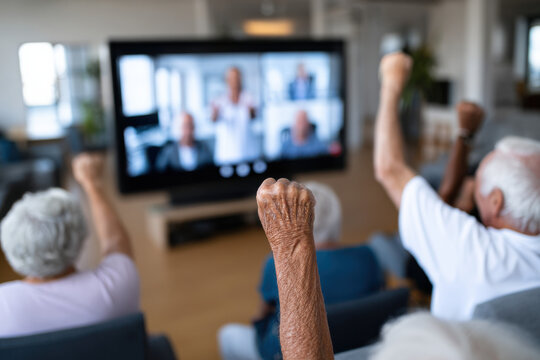 Group of seniors in group video call with physiotherapist demonstrating gentle rehabilitation exercises, participants follow from home, concept of group tele-physiotherapy and social engagement