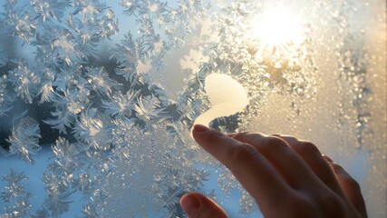 Hand tracing patterns on frost-covered window with sunlight shining - Powered by Adobe