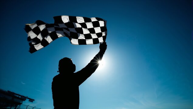 Silhouette race official waves finish line checkered flag under sunny sky