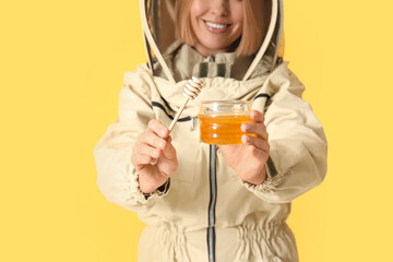 Female beekeeper with jar of sweet honey and dipper on yellow background