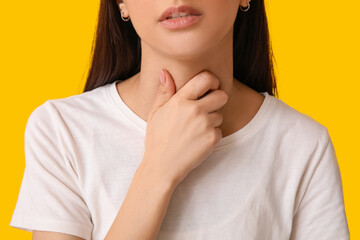 Young woman suffering from sore throat on yellow background, closeup
