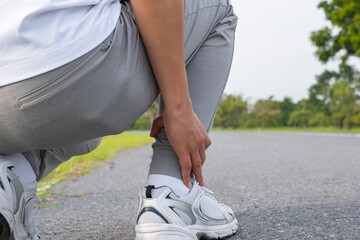 Asian man gripping painful ankle during morning run—outdoor injury, muscle strain, and joint...