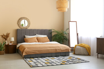 Cozy bed, mirror and lamp on bedside table in beautiful bedroom