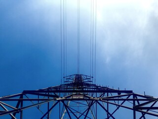 Electricity transmission tower silhouette with power lines against blue sky, looking up view symbolizing energy, infrastructure, and power industry.