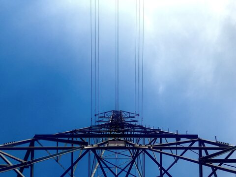 Electricity transmission tower silhouette with power lines against blue sky, looking up view symbolizing energy, infrastructure, and power industry.
