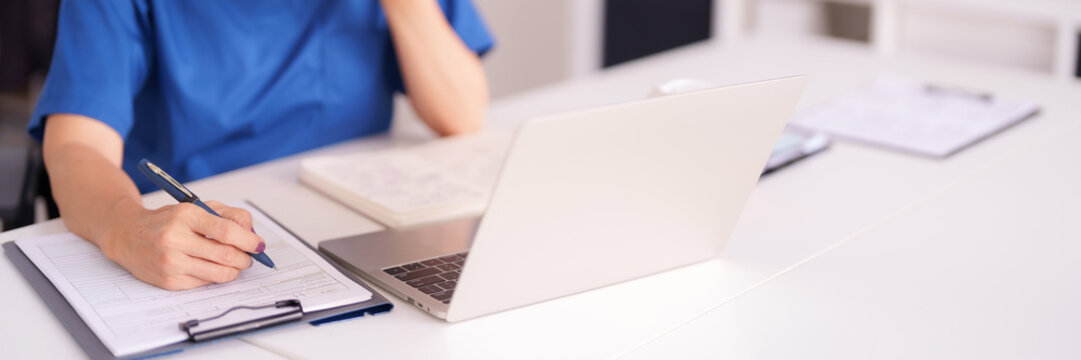 Healthcare Professional Documenting Patient Notes Laptop Work Desk Medical Clinic Office Environment