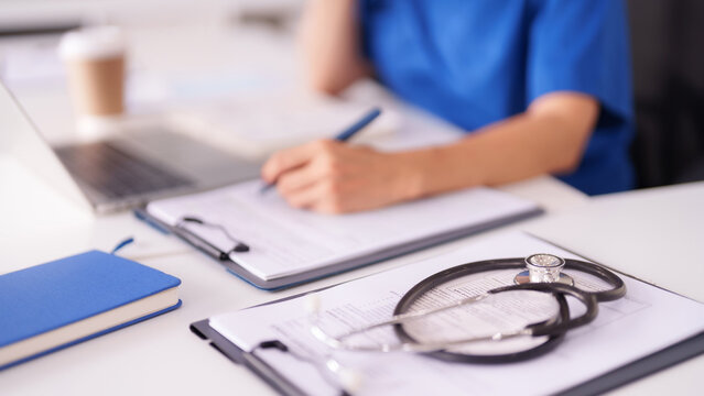 Female doctor medical professional records patient information on clipboard laptop in modern clinic office healthcare setting for patient care documentation - Powered by Adobe
