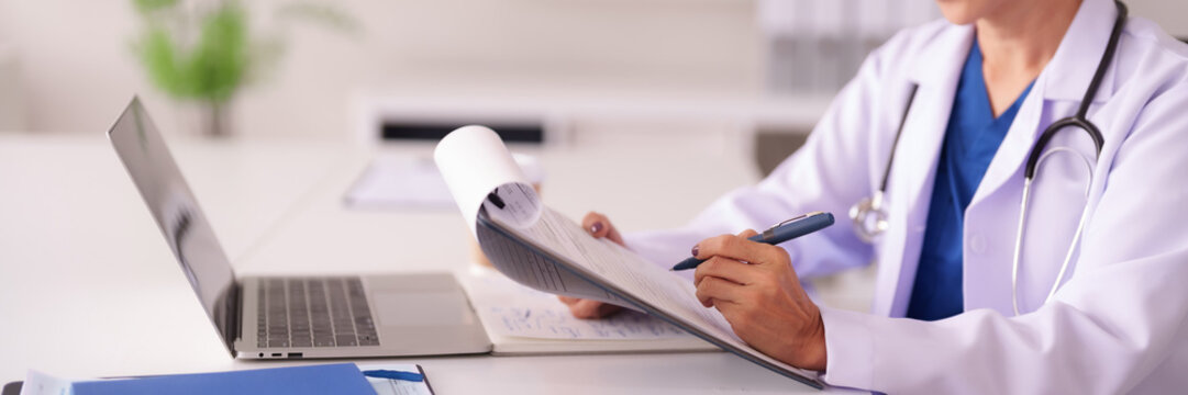 Asian adult female doctor physician medical professional documents patient chart notes healthcare provider uses laptop computer clinic office setting - Powered by Adobe