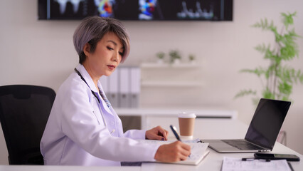 Asian Doctor Writing Patient Notes in Modern Medical Office Focused on Professional Healthcare...