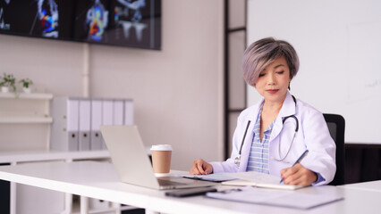 Asian female doctor writes patient notes in modern clinic office studying medical imaging professional healthcare consultant diligently documenting patient records