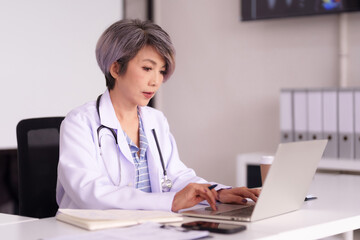 Asian adult female doctor healthcare professional working laptop computer modern medical office...