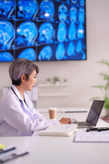 Asian female doctor healthcare professional analyzing patient brain scans on laptop in modern medical office research facility for diagnostics