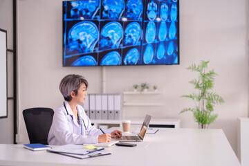 Asian female doctor reviewing brain scans on screen with laptop technology in modern medical office...