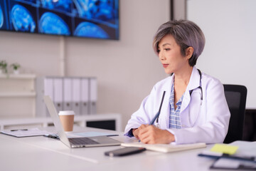 Asian adult female physician diligently reviews medical scans patient data on laptop computer in a professional healthcare clinic office
