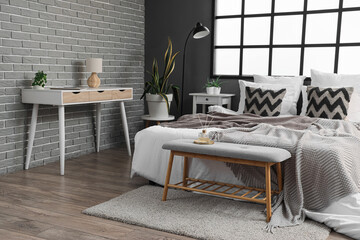 Interior of modern bedroom with cozy bed and reed diffuser on grey bedside bench