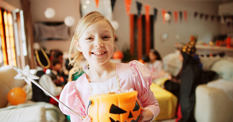 Bucket, halloween and portrait of happy girl child in living room of home for celebration of holiday. Candy, costume and smile of excited kid fairy in apartment for Autumn tradition of trick or treat