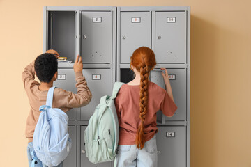 Teenage students opening locker on beige background, back view