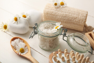 Composition with spa stones, massage body brush, chamomile flowers and jar of sea salt on white...