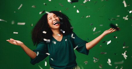 Happy woman, winning and laughing with confetti in studio for party on a green background. Excited, female person or model with smile in celebration for festive surprise, bonus prize or lottery