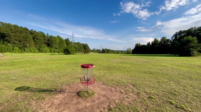 Disc golf basket in open meadow with distant power lines and forest edge in Tukums, Latvia