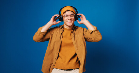 Studio, dancing and man with headphones, music or listening to audio with tech, streaming or online. Blue background, space and person with smile for playlist, rhythm and happy for song on radio