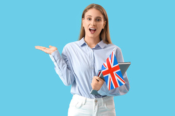 Surprised female English teacher with UK flag and notebooks showing something on blue background