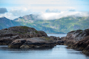 Rocks in shallow water with distant mountains across fjord in Lofoten, in Northern Norway