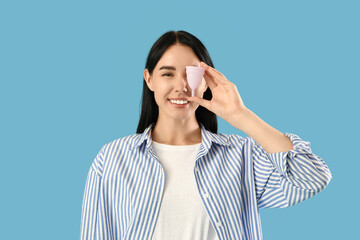 Young woman with menstrual cup on blue background