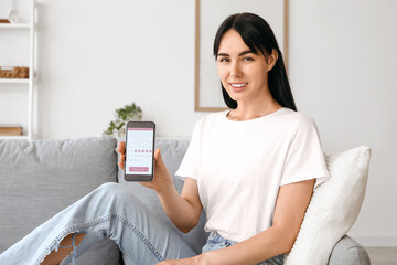 Young woman holding mobile phone with menstrual calendar at home