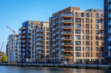 Modern apartment buildings line a riverbank under a clear sky